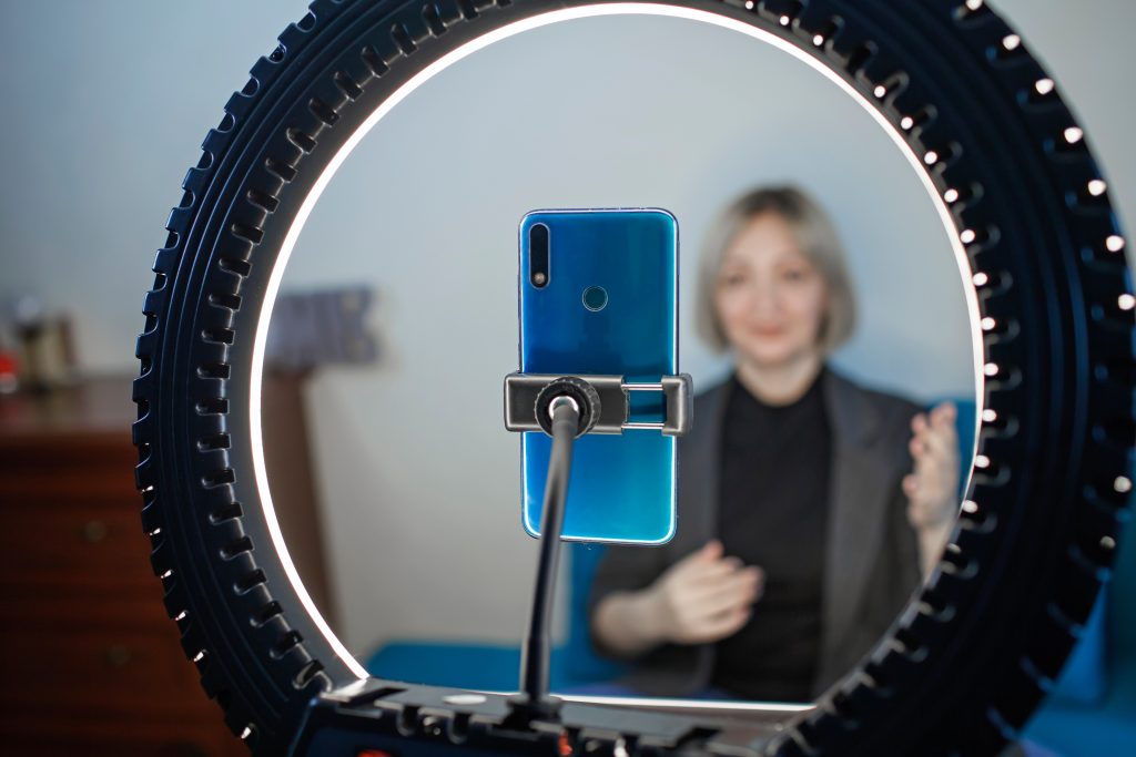 Woman talking to camera and recording video with smartphone and ring light lamp at home